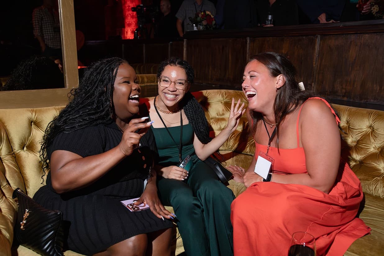 Three guests laughing together on a gold velvet sofa